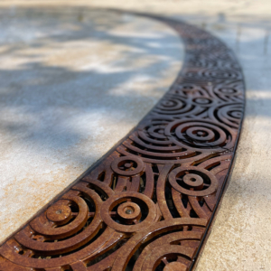 Cast iron radius trench grate in decorative Oblio pattern from Iron Age Designs. Installed in splash park.