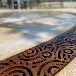 Cast iron radius trench grate in decorative Oblio pattern from Iron Age Designs. Installed in splash park.