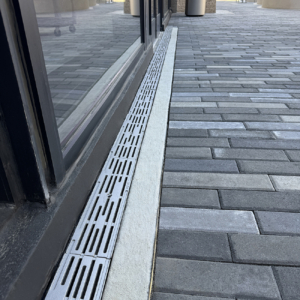 Cast iron trench grate in decorative Rain pattern from Iron Age Designs. Installed in building entryway.