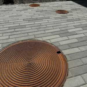 Raw cast iron manhole covers in decorative Bullseye pattern from Iron Age Designs. Installed in courtyard with pavers.