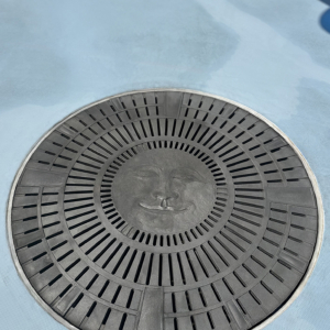 Cast aluminum catch basin grate in decorative Moon Face pattern by Iron Age Designs.