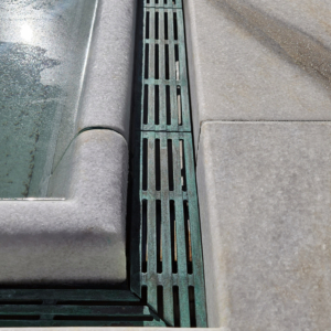 Cast bronze trench grates in water feature, aged 7 years, showing verdigris finish. Que pattern by Iron Age Designs.