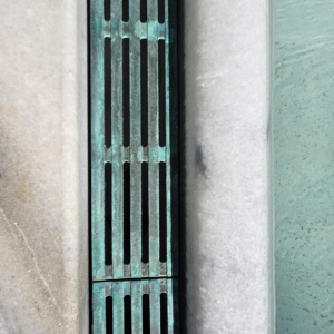 Cast bronze trench grates in water feature, aged 7 years, showing verdigris finish. Que pattern by Iron Age Designs.