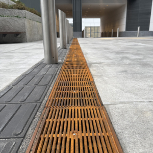 Cast iron Que trench grates by Iron Age Designs installed next to directional wayfinding tiles.