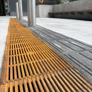 Cast iron Que trench grates by Iron Age Designs installed next to directional wayfinding tiles.