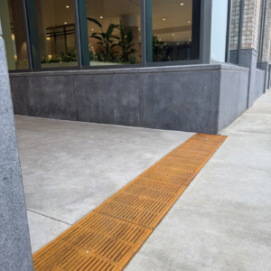 Cast iron Que trench grates by Iron Age Designs installed near building entryway.